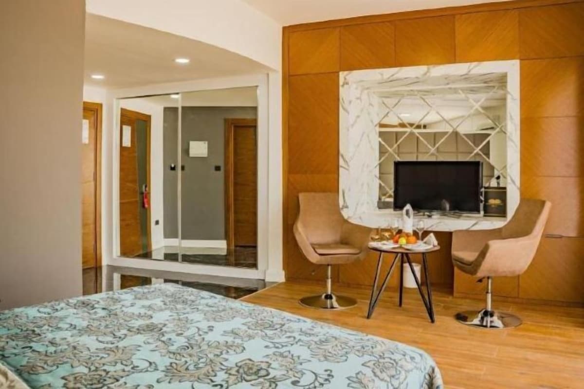 A hotel room with a bed, a television, a small table with fruit, and two chairs.