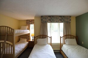 A room with two single beds, a bunk bed, a nightstand, and a window with curtains. - 2 bedroom condo sleeping 8 at Inns of WV (Waterville Valley)