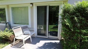 En overdækket terrasse med bænk, skydedør og et lille haveområde.