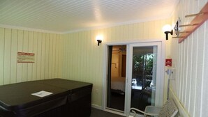 Et spa-værelse med jacuzzi, bænk og en skydedør, der fører ud til en balkon.
