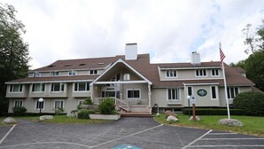 A two-story building with a central entrance, a parking lot with handicapped accessibility, and an American flag. - One Bedroom at Inns of Waterville Valley (Waterville Valley)