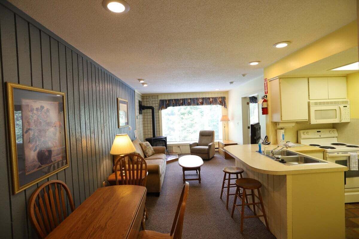 A compact living space with a kitchenette, a dining area with a table and chairs, a sofa, and a small island with stools.