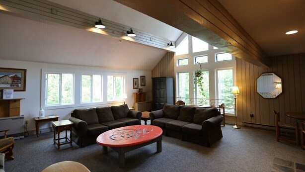 A spacious living room with a high ceiling, large windows, and a fireplace. - One Bedroom at Inns of Waterville Valley (Waterville Valley)