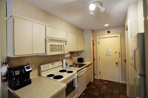 A compact kitchen with a microwave, stove, coffee maker, and a refrigerator.