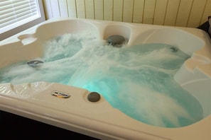 A hot tub with a control panel, a drain, and a view of a window with blinds.
