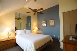 Ein Hotelzimmer mit einem Bett, zwei Nachttischlampen, einem Deckenventilator, einem Spiegel und gerahmten Bildern an der Wand.