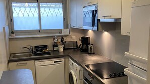 A compact kitchen with a dishwasher, washing machine, stove, and microwave. - Ground Floor 3-Room Apartment with Terrace & Garden, 5 min to Beach, A/C, Parking, Villeneuve-Loubet (Villeneuve-Loubet)