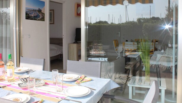 A dining area with a table set for four, a glass partition, and a view of the outdoors. - Ground Floor 3-Room Apartment with Terrace & Garden, 5 min to Beach, A/C, Parking, Villeneuve-Loubet (Villeneuve-Loubet)