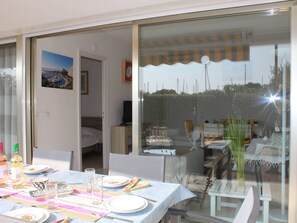 A dining area with a table set for four, a glass partition, and a view of the outdoors. - Ground Floor 3-Room Apartment with Terrace & Garden, 5 min to Beach, A/C, Parking, Villeneuve-Loubet (Villeneuve-Loubet)