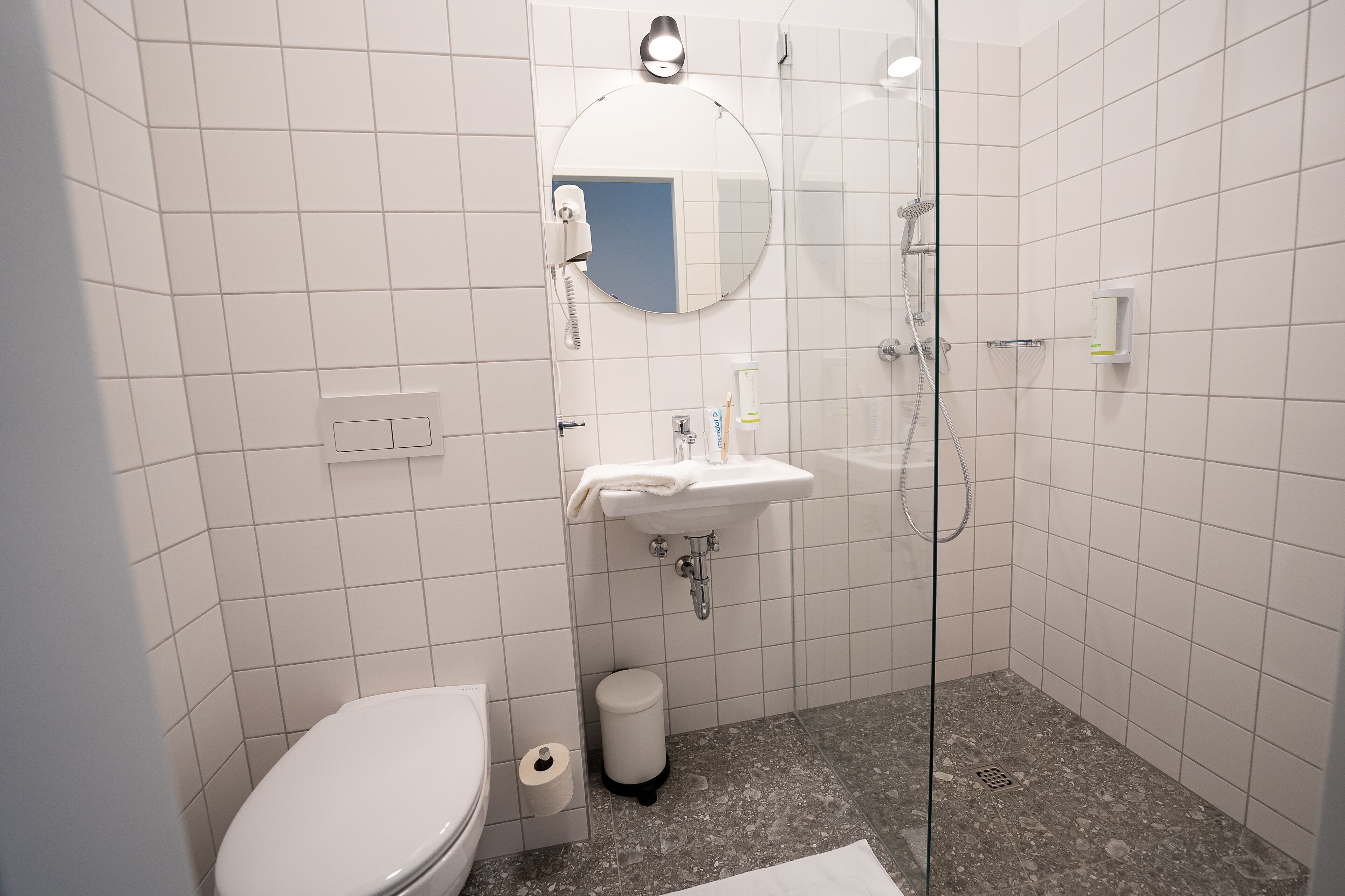 A bathroom with a toilet, sink, mirror, and shower.