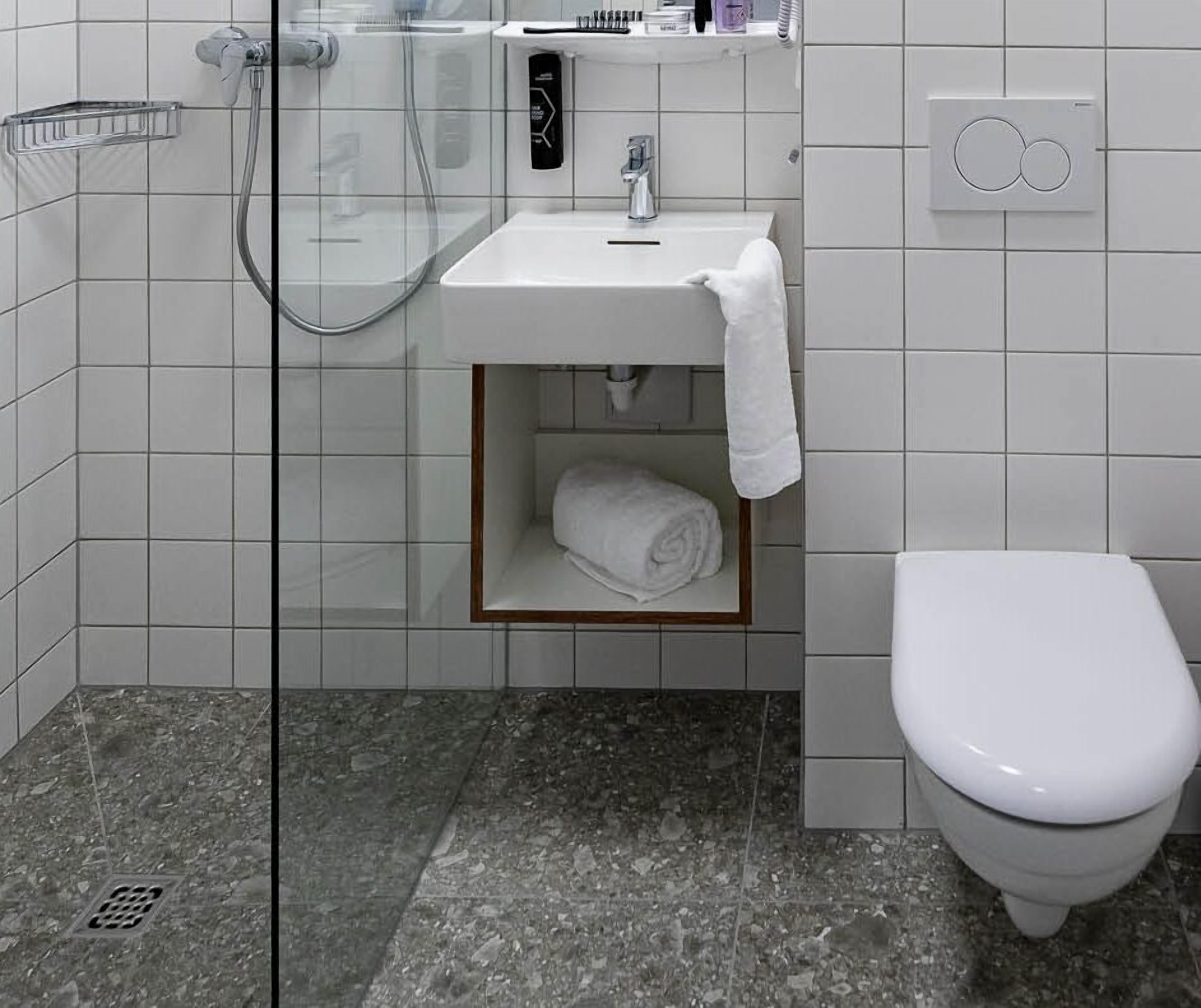 A modern bathroom with a glass shower enclosure, a white sink with a towel rack, and a toilet.