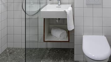 Un baño moderno con cabina de ducha de vidrio, un lavamanos blanco con toallero y un inodoro.
