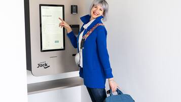 Una persona utilizza una postazione self check-in etichettata 'Jack' in una stanza con tappeto nero e parete bianca.