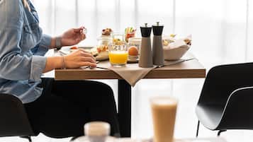Una escena de desayuno con una mesa lista para dos personas, incluyendo un vaso de jugo de naranja, una taza de café y diversos alimentos para el desayuno.