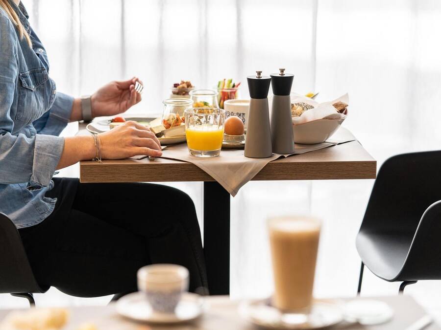 Una escena de desayuno con una mesa lista para dos personas, incluyendo un vaso de jugo de naranja, una taza de café y diversos alimentos para el desayuno.