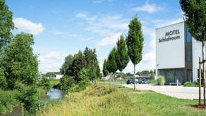 Ein modernes Gebäude mit der Aufschrift 'Motel Schlafröm', einem Parkplatz und einem Fluss im Hintergrund.
