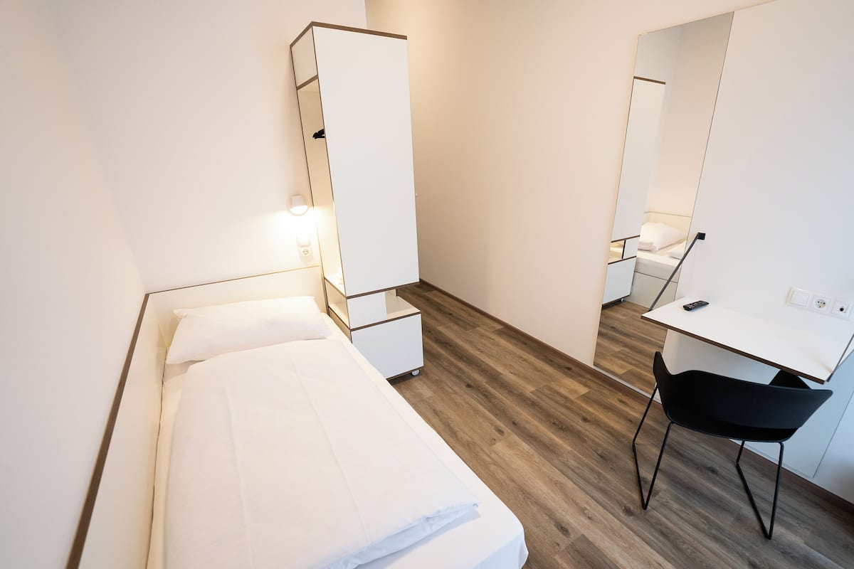 Une petite chambre à coucher moderne, équipée d’un lit, d’un bureau et d’une chaise.