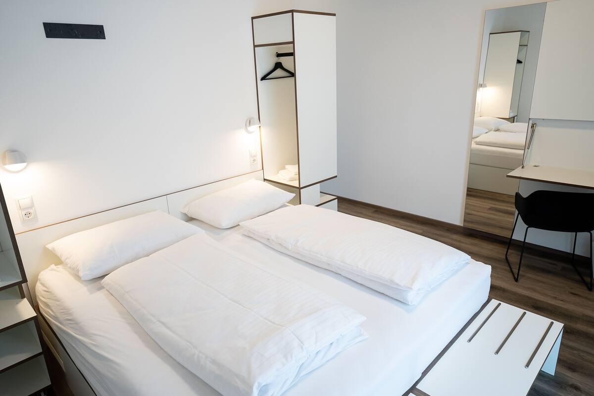 Une chambre d’hôtel avec deux lits, un bureau, une chaise, un miroir et une armoire.