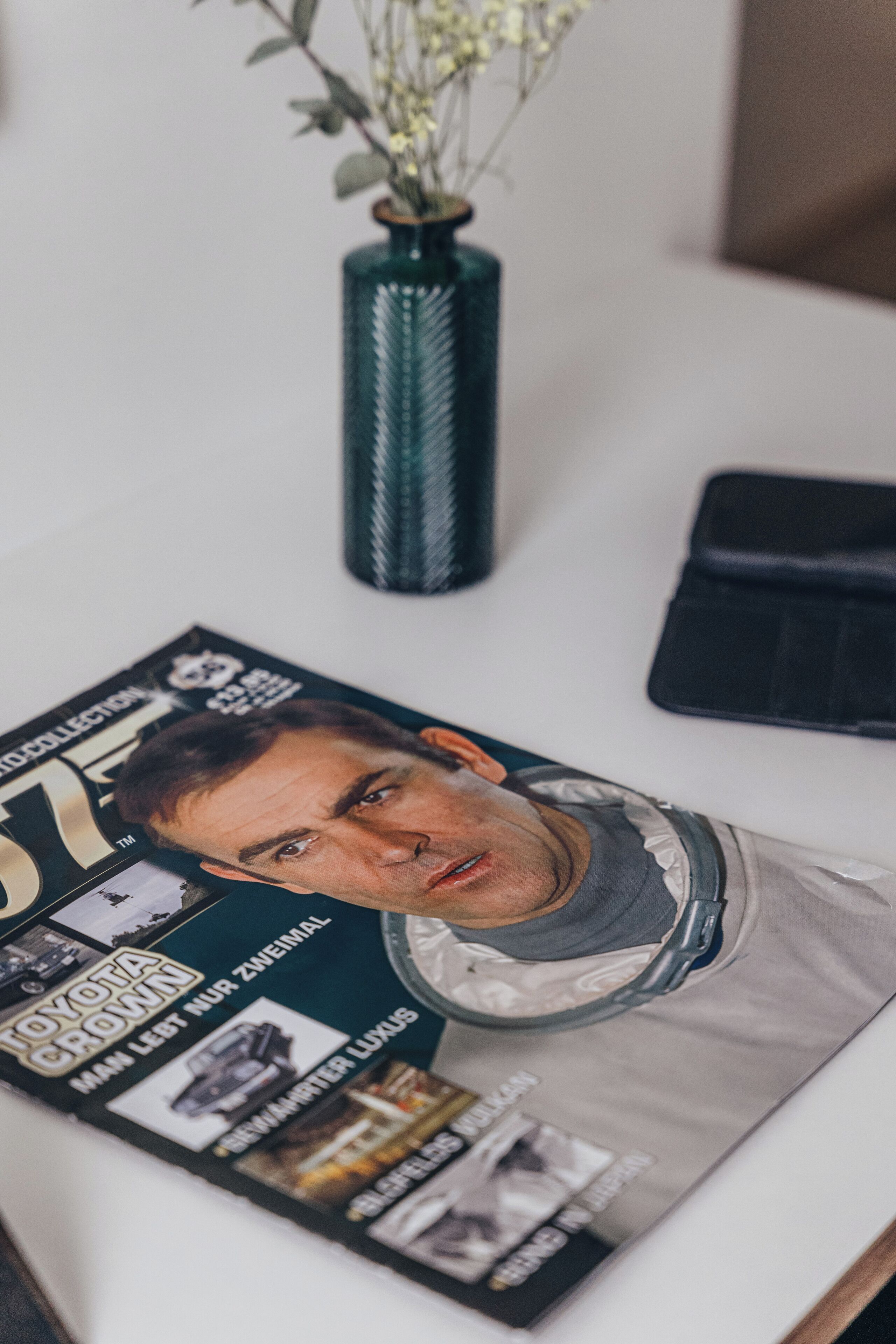 A magazine on a table with a vase of flowers.