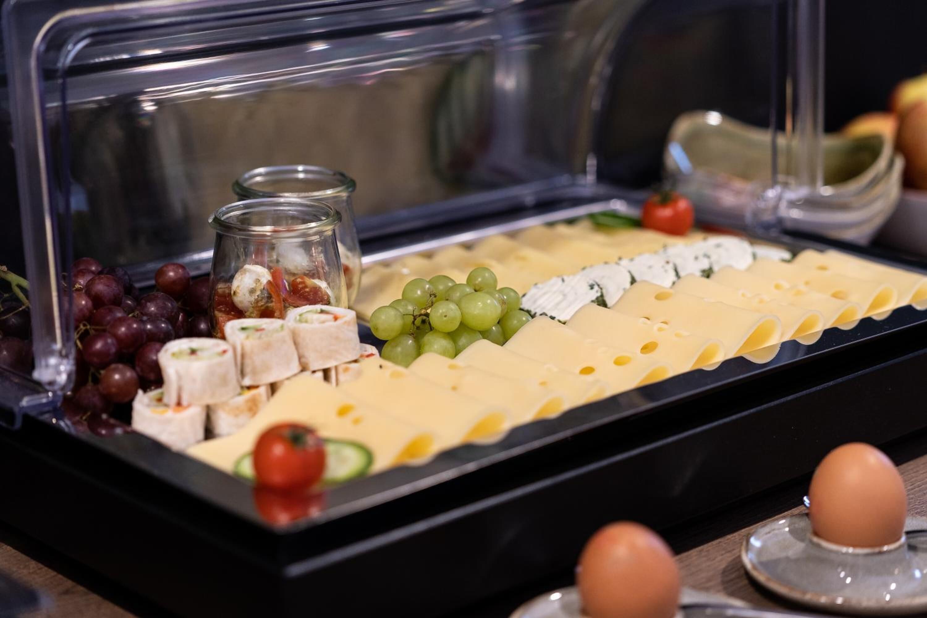 A buffet with various cheeses, grapes, and small jars of spreads.
