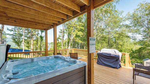 Een houten terras met een jacuzzi, een barbecue en een schommelset.