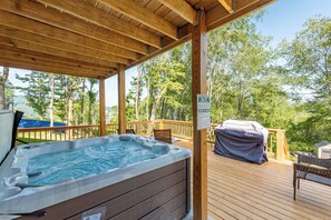 A wooden deck with a hot tub, a barbecue grill, and a swing set.