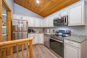 A kitchen with white cabinets, stainless steel appliances, a wooden ceiling, and a granite countertop.