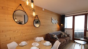 A dining area with a wooden wall, a round table set with white plates and glasses, and a brown sofa with patterned cushions. - Avoriaz - Beautiful renovated apt for 4 people with wifi (Avoriaz)