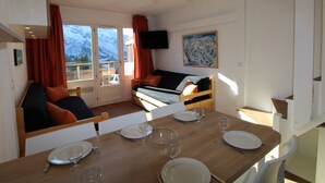 A dining area with a wooden table set for four, a sofa with cushions, and a television mounted on the wall.