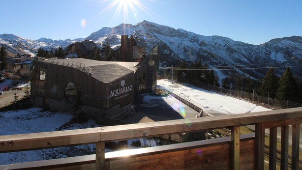 A wooden building with the name 'AQUARIAZ' in the foreground, surrounded by snow-covered mountains and a clear sky.