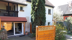 Uma casa com telhado de telhas vermelhas, portão de madeira e entrada com calçada.