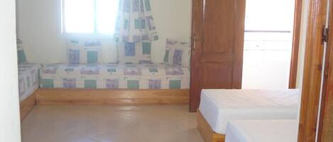 A room with two beds, a wooden door, and a window with a curtain.