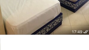 Twee eenpersoonsbedden met blauwe hoofdborden en witte beddengoed in een kamer met een blauwe deur en een kleine airconditioning aan de muur.