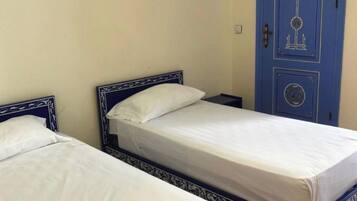Two single beds with blue headboards and white bedding in a room with a blue door and a small air conditioning unit on the wall.