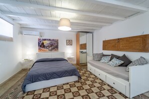 A bedroom with a bed, a sofa, a patterned carpet, a painting, and a wooden headboard.