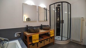 Un bagno con una vasca, un mobiletto in legno con due lavabi in pietra, una cabina doccia in vetro e un portasciugamani con asciugamani gialli.