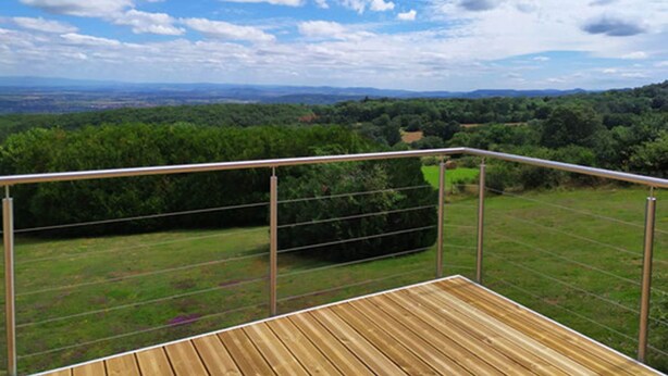 Un pontile in legno con ringhiera metallica affacciato su un paesaggio verde e colline lontane.