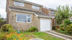 A two-story house with a garage, surrounded by a well-maintained garden with various plants and flowers. - 4-bed Detached, Pet Friendly House in Nelson (Nelson)