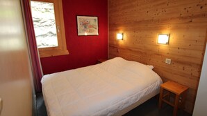 A bedroom with a wooden wall, a bed, a small wooden stool, and two wall-mounted lights. - Avoriaz - Duplex for 6 with balcony and WIFI (Avoriaz)