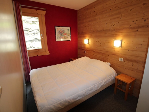 Un dormitorio con pared de madera, una cama, un taburete pequeño de madera y dos luces fijadas a la pared.