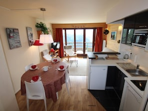 Un espacio habitable compacto con comedor, cocina y balcón con vistas.