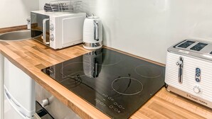 A compact kitchen with a built-in stove, a toaster, and a kettle on a wooden countertop. - The Rosebery Retreat By The Castle 1-bed Apartment (Inverness)