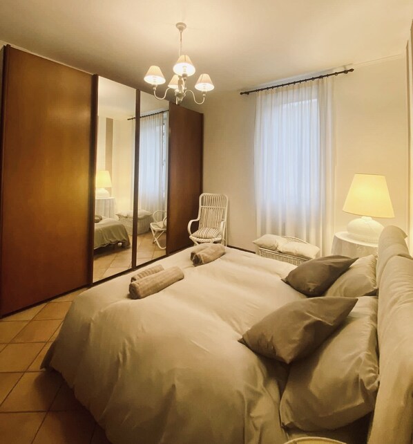 Relax in this serene space with a large bed, a comfortable chair, and a small table with a lamp.