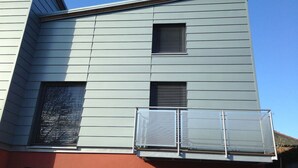 A multi-story building with horizontal siding, a balcony with metal railings, and a red lower section. - Contemporary bolthole, short walk from City Sleeps 2+1 (Canterbury)