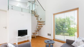 A modern living room with a staircase, a television, a sofa, and a large window with blinds. - Contemporary bolthole, short walk from City Sleeps 2+1 (Canterbury)
