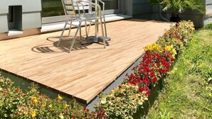 A modern house with a wooden deck, a glass door, and a small garden with colorful flowers. - Contemporary bolthole, short walk from City Sleeps 2+1 (Canterbury)