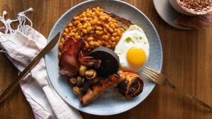 Een bord met ontbijtproducten, waaronder bonen, spek, worstjes, champignons, een gebakken ei en toast.
