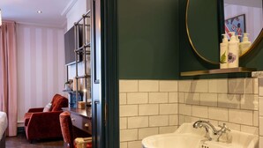 Hotelkamer met een groot bed, een rode fauteuil, een houten dressoir, een witte wasbak en een spiegel met toiletartikelen.