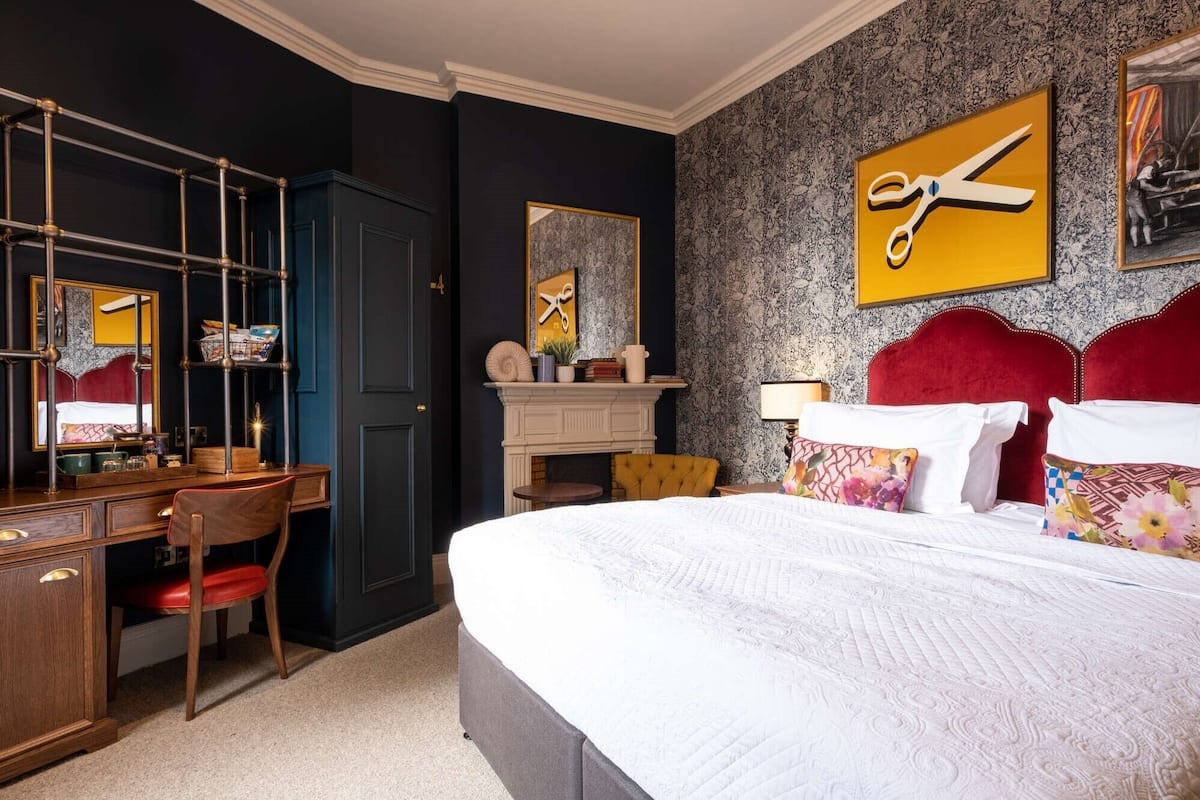 A hotel room with a large bed, a desk, a chair, a dresser, and a mirror.