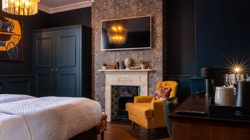 Una habitación de hotel con una cama grande, un sillón amarillo, una chimenea y un televisor montado en la pared.